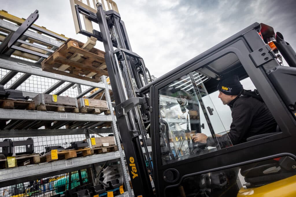 Operator driving a Yale Forklift lifting pallets outdoors in racking safely.